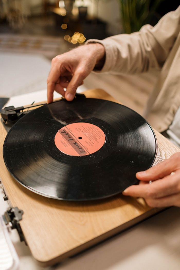get-in-touch Close-up of hands placing a vinyl record on a vintage turntable indoors.