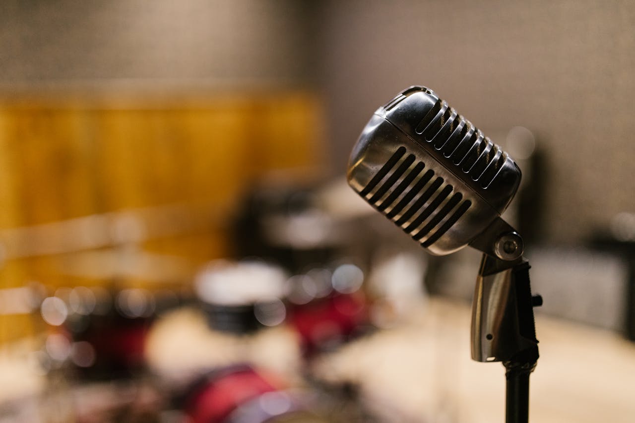 about-us Close-up of a vintage microphone in a music studio with blurred drum set in the background.